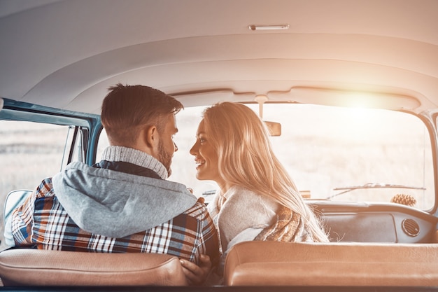 Vista trasera de la hermosa joven pareja disfrutando de un viaje por carretera juntos mientras está sentado en los asientos delanteros de la minivan