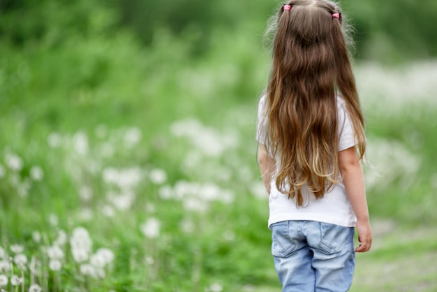 Vista trasera de una hermosa niña en una camiseta y jeans en un campo cerca del bosque