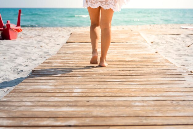 Vista trasera de hermosas piernas de mujer caminando en verano en un muelle de madera en la playa Vacaciones de verano tropical vacaciones personas concepto estilo de vida Turista disfrutando del sol y el agua azul actividad de ocio