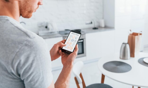 Vista trasera de un hombre adulto que está adentro controlando la tecnología del hogar inteligente