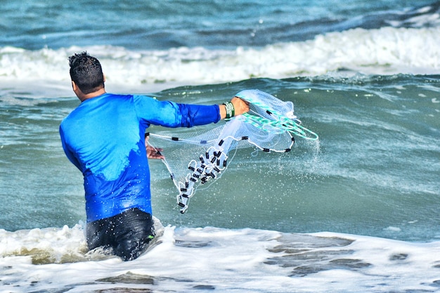 Foto vista trasera de un hombre arrojando una red de pesca en el mar