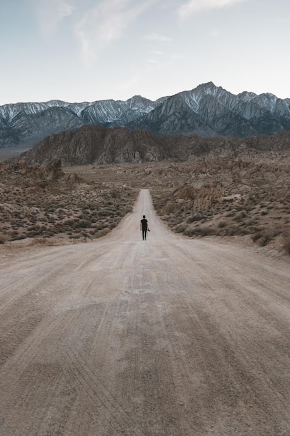 Vista trasera de un hombre caminando por un camino de tierra contra el cielo
