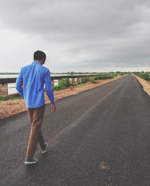 Foto vista trasera de un hombre caminando por la carretera contra el cielo