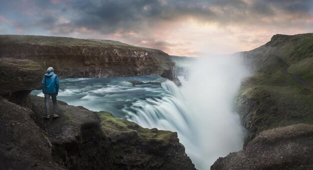 Vista trasera de un hombre caminando en la cascada de Gullfoss durante la puesta de sol