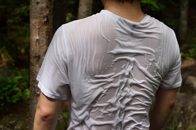 Foto vista trasera del hombre con camiseta húmeda de pie en el bosque