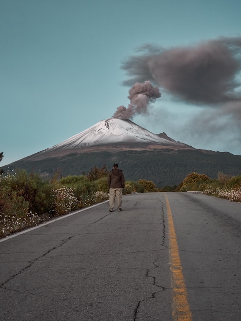 Foto vista trasera de un hombre en la carretera contra el humo que emite el volcán y el cielo