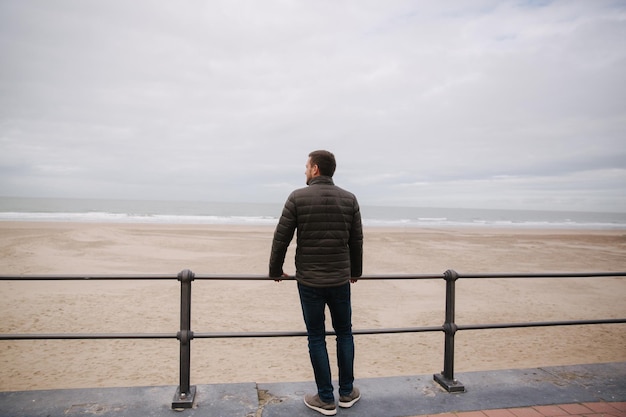 Foto vista trasera del hombre con chaqueta caqui mirando el mar del norte