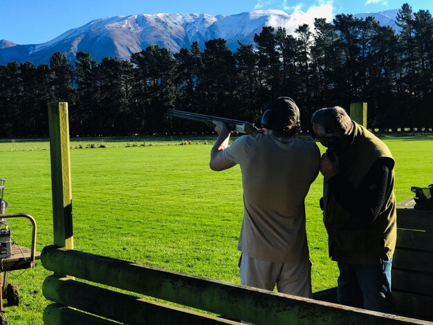 Foto vista trasera de un hombre disparando arcilla contra la montaña