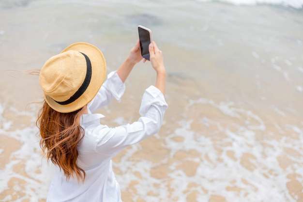 Vista trasera de un hombre fotografiando con un teléfono móvil en la playa