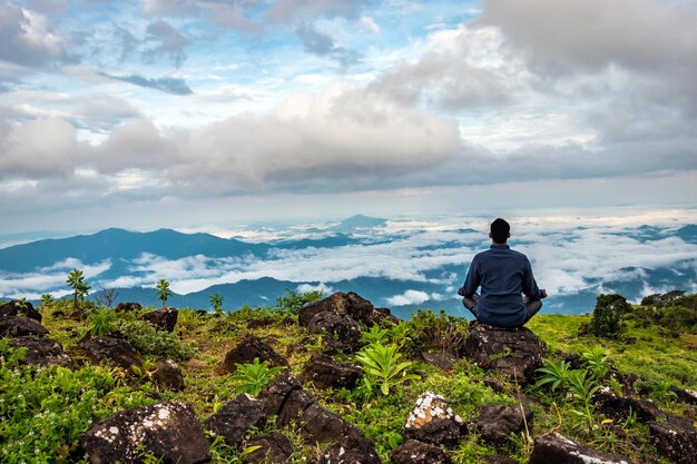 Vista trasera de un hombre haciendo meditación en una roca con una montaña prístina con una espectacular vista del cielo