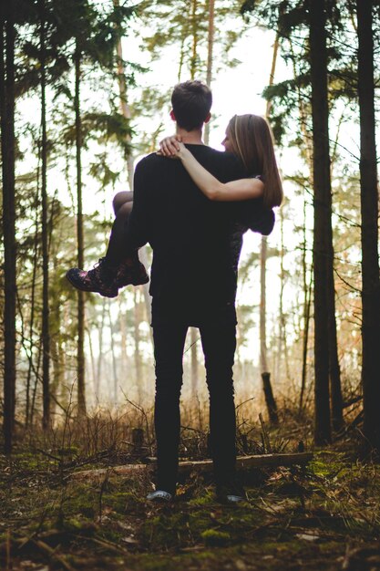 Vista trasera de un hombre levantando a su novia en el bosque