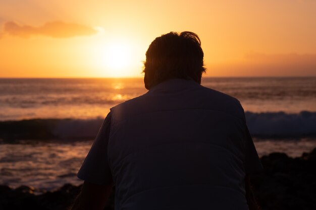 Vista trasera del hombre maduro en el mar mirando el horizonte y la luz naranja del atardecer