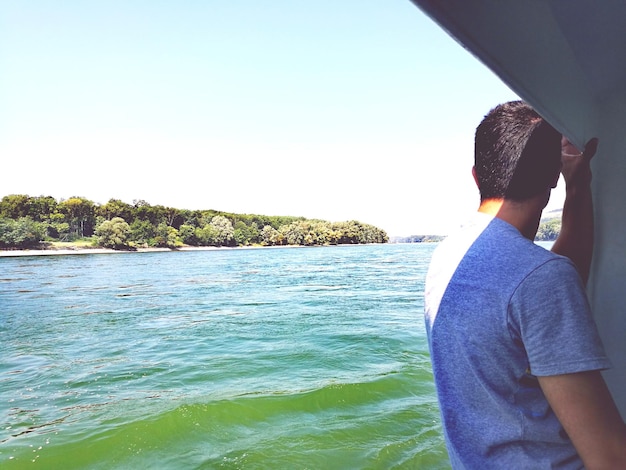 Vista trasera de un hombre mirando al mar contra un cielo despejado