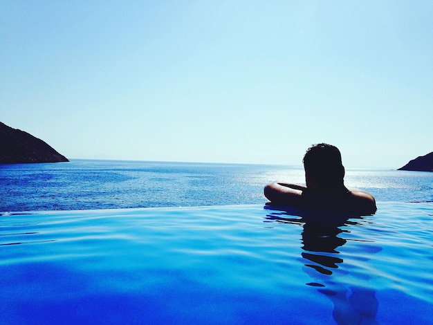 Foto vista trasera de un hombre mirando al mar mientras nada en una piscina infinita