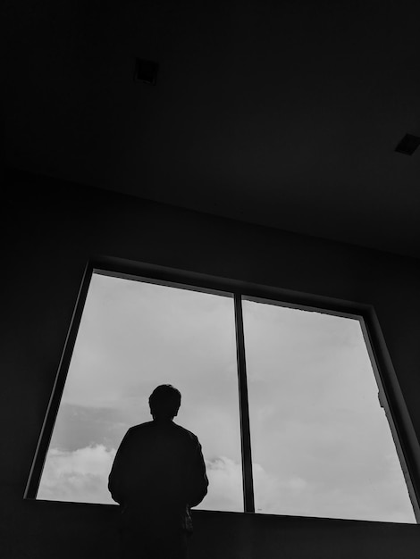 Foto vista trasera del hombre mirando a través de la ventana mientras está de pie en la habitación