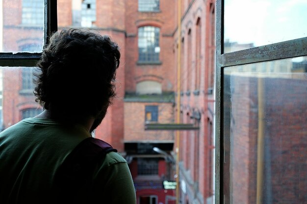 Vista trasera de un hombre mirando por la ventana