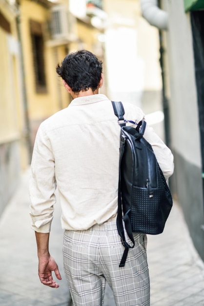 Vista trasera de un hombre con mochila caminando por un callejón en la ciudad