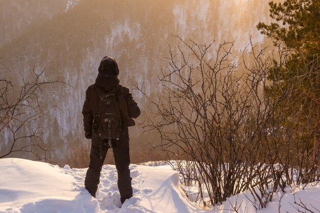 Vista trasera de un hombre en una montaña mirando a lo lejos en los rayos del sol poniente. Escalando en las montañas