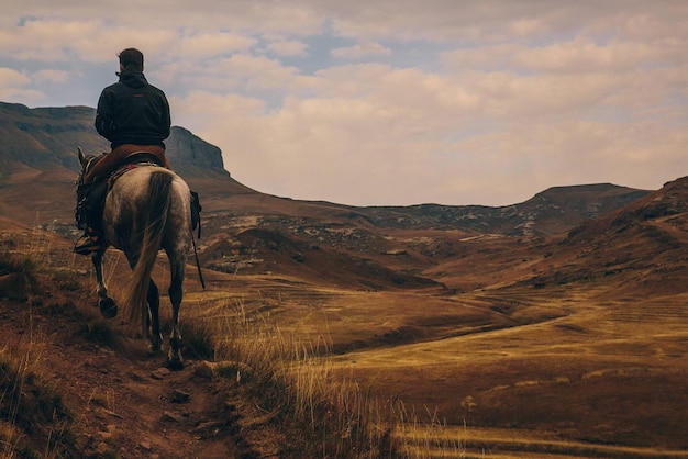 Vista trasera de un hombre montando a caballo en la montaña contra el cielo