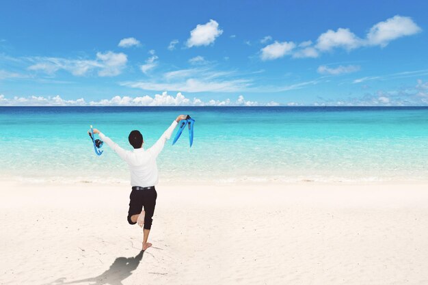 Vista trasera del hombre de negocios feliz corriendo en la playa