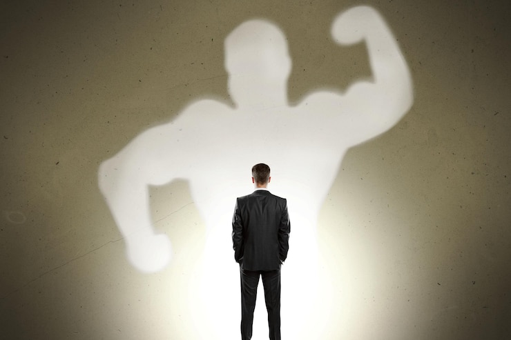 Foto vista trasera del hombre de negocios con fuerte sombra muscular de pie sobre fondo de pared gris concepto de confianza y fuerza