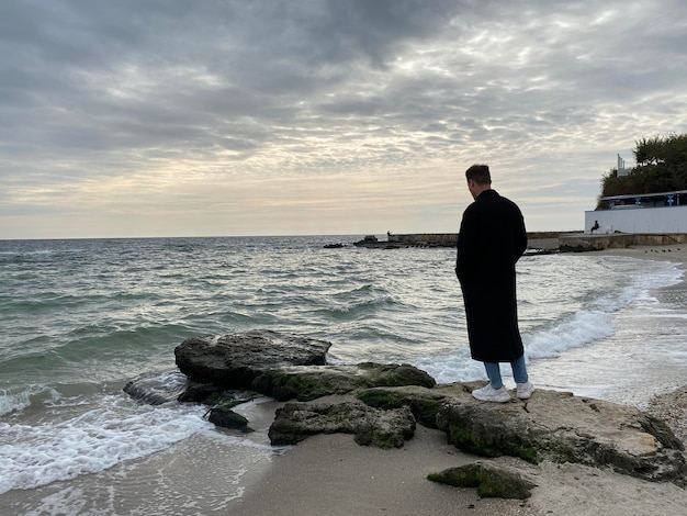 Vista trasera de un hombre parado solo en la playa mirando el mar