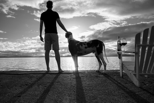 Foto vista trasera de un hombre con un perro de pie junto al mar contra el cielo