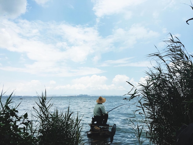 Vista trasera de un hombre pescando mientras está sentado en las rocas del lago