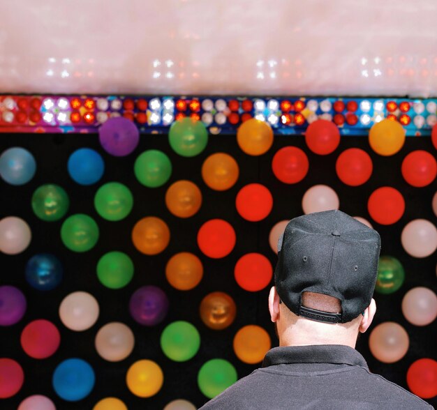 Vista trasera de un hombre de pie contra globos de colores en la pared