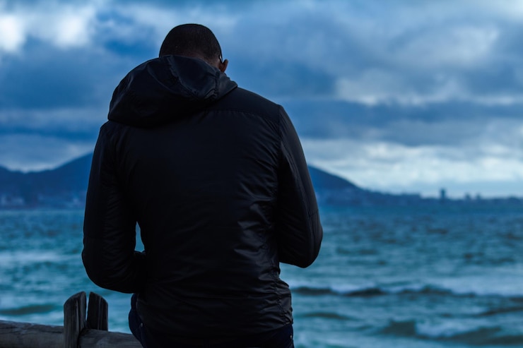 Foto vista trasera de un hombre de pie junto al mar contra un cielo nublado