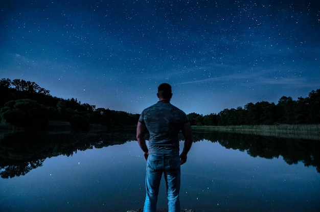 Foto vista trasera de un hombre de pie en el lago contra el cielo por la noche