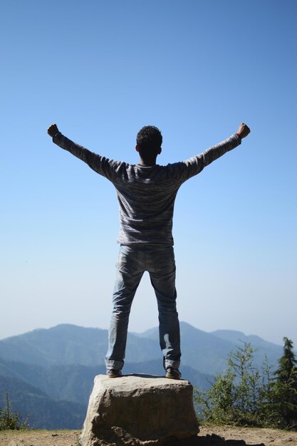 Vista trasera de un hombre de pie en la montaña contra el cielo azul