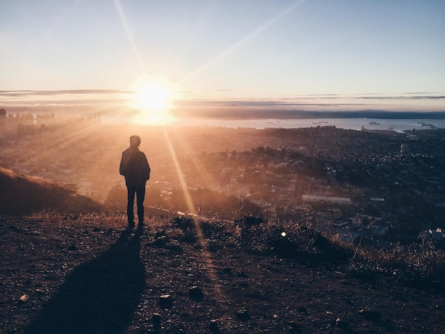 Foto vista trasera de un hombre de pie en la montaña contra un cielo brillante durante la puesta de sol