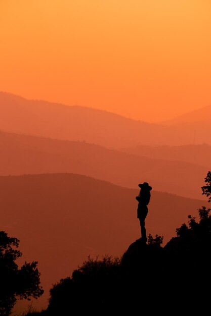 Vista trasera de un hombre de pie en la montaña contra el cielo durante la puesta de sol