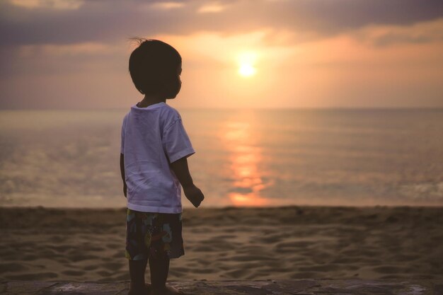 Foto vista trasera de un hombre de pie en la playa durante la puesta de sol