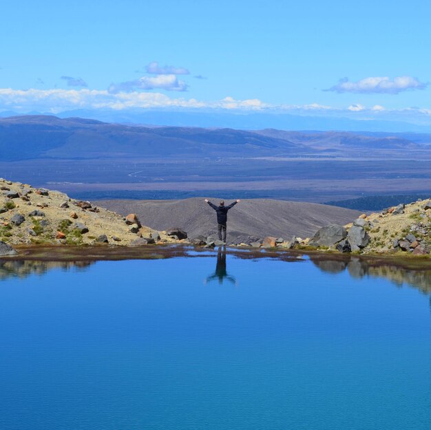 Foto vista trasera de un hombre de pie en una roca junto al lago contra el cielo azul