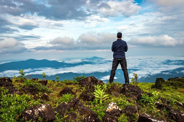 Foto vista trasera de un hombre de pie en una roca con una montaña prístina con una espectacular vista del cielo