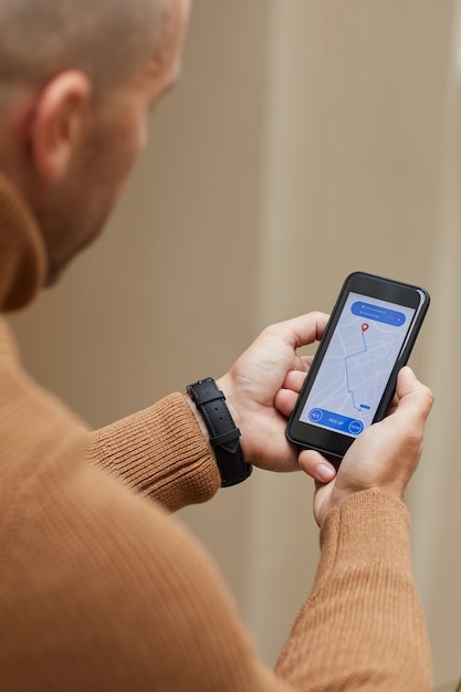 Vista trasera del hombre que sostiene el teléfono móvil y sigue el coche en el mapa esperando el taxi