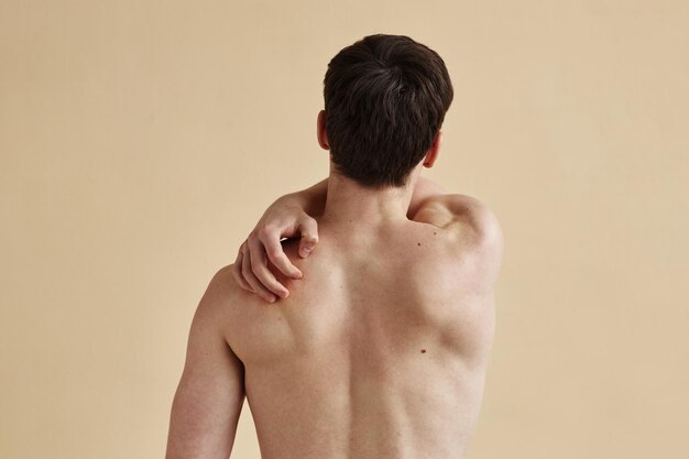 Vista trasera de un hombre rascándose la espalda desnuda
