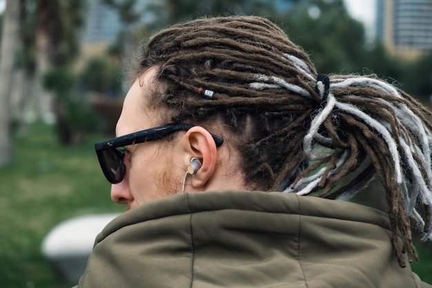 Foto vista trasera del hombre con rastas escuchando música con auriculares o audífonos al aire libre cerrar