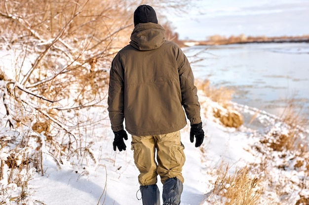 Vista trasera del hombre en ropa de abrigo caminando en la naturaleza nevada en invierno descansar disfrutar de un estilo de vida activo chico guapo caminar a lo largo de campos nevados en el día de invierno congelado solo al aire libre viajes de caminata bushcraft