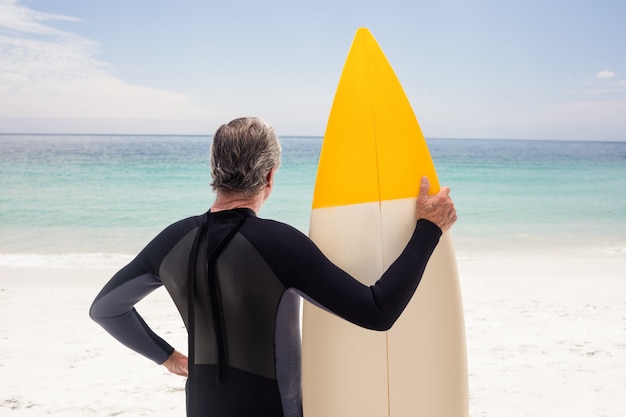 Vista trasera del hombre senior en traje de neopreno con una tabla de surf