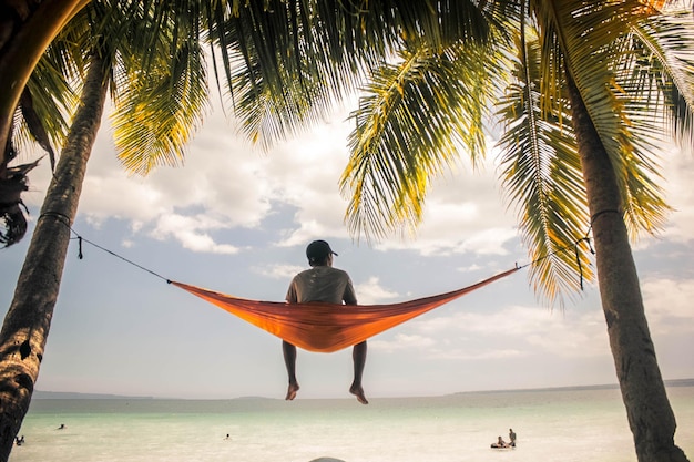 Vista trasera de un hombre sentado en una hamaca en la playa contra un cielo nublado