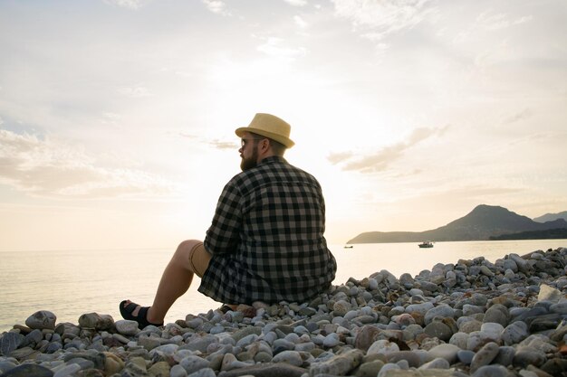 Vista trasera del hombre sentado en la playa en un día soleado fuera de vacaciones de fondo o concepto de viaje independiente