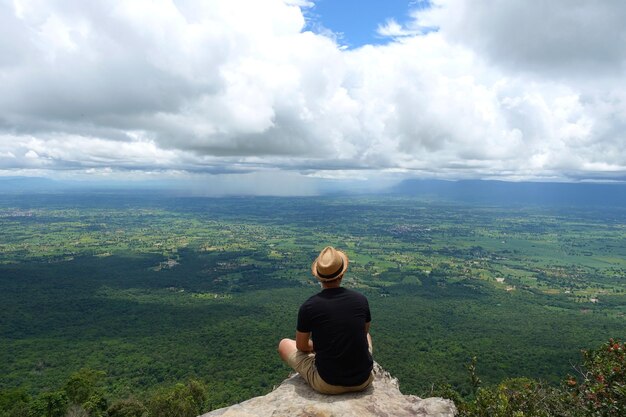 Vista trasera de un hombre sentado sobre el paisaje contra el cielo