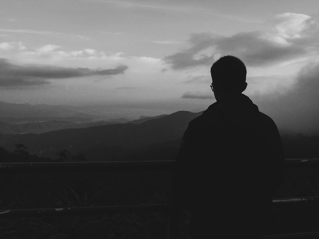 Vista trasera de un hombre en silueta mirando las montañas contra el cielo durante la puesta de sol