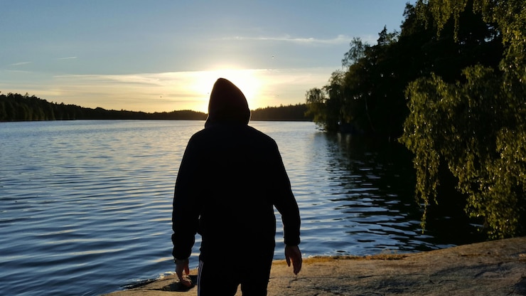 Foto vista trasera de un hombre en silueta de pie junto al lago contra un cielo nublado durante la puesta de sol