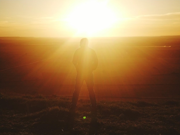 Foto vista trasera de un hombre en silueta de pie en la montaña contra el sol brillante durante la puesta de sol