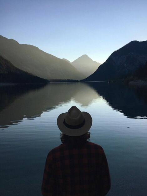 Foto vista trasera de un hombre con sombrero mientras mira el lago contra el cielo