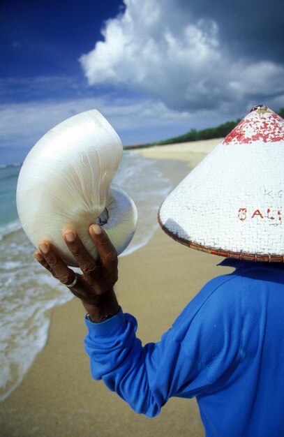 Foto vista trasera de un hombre sosteniendo una concha de mar en la playa contra el cielo